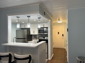 A compact kitchen with white cabinets, a stainless steel refrigerator, a microwave, and an oven. There are two pendant lights above the island.