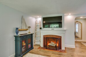 Una sala de estar con chimenea, un televisor montado encima y un mueble decorativo con un velero en la parte superior.