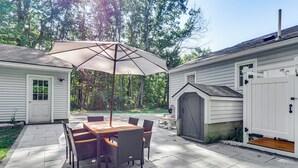 En terrasse med et bord, stole og en stor parasol, samt et lille skur.