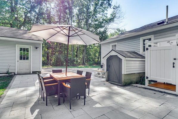 A patio with a table and chairs, a large umbrella, and a small shed. - Near Beach: Coastal Maine Getaway w/ Yard (Wells)