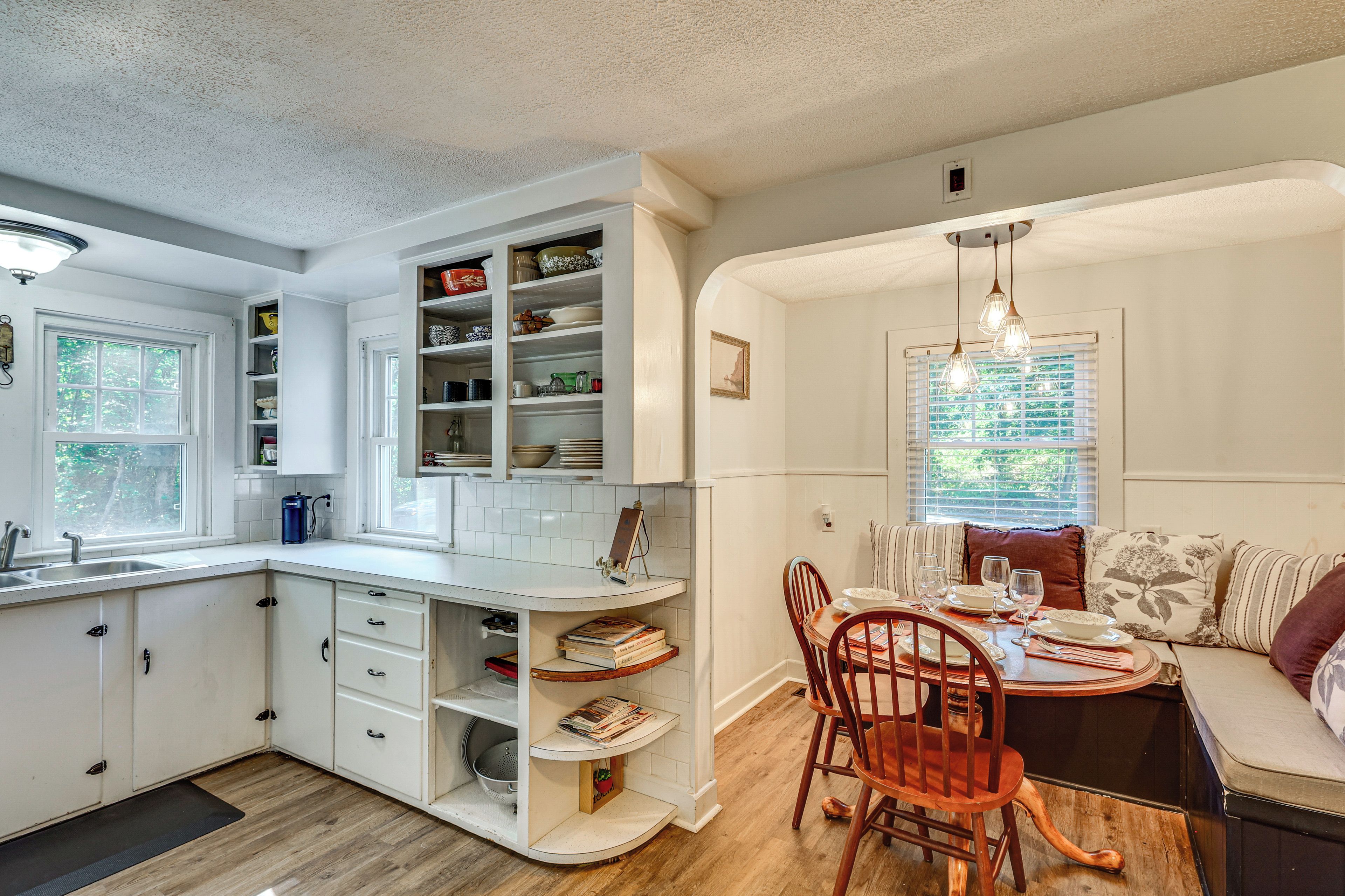A kitchen with white cabinetry, a dining area with wooden chairs, and a window with blinds.