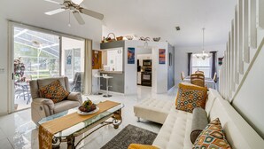 Ein modernes Wohnzimmer mit Sofa, Sessel und Couchtisch. Im Hintergrund befindet sich eine Küchenzeile mit Esstisch und Stühlen.
