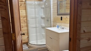 A wooden-paneled bathroom with a glass shower enclosure, a white sink, and a toilet. - White cabin in the woods close to Univ. of Central Missouri and Whiteman AF Base (Warrensburg)