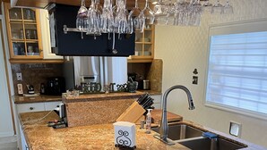 Uma cozinha com bancadas de granito, uma pia de aço inoxidável e taças de vinho penduradas.
