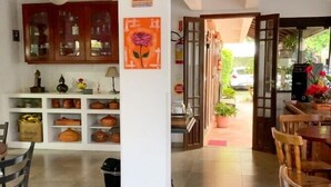 A spacious room with a dining area, a kitchen with shelves of pottery, and a view of the outdoors. - Dell osky Pousada (Florianópolis)