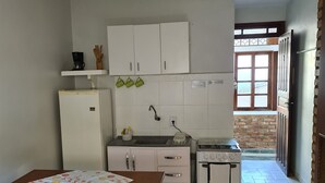 A compact kitchen with white cabinets, a refrigerator, a stove, and a dining table with a bench. - Dell osky Pousada (Florianópolis)