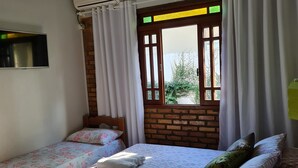 A room with two single beds, a ceiling fan, an air conditioning unit, a window with curtains, and a brick wall. - Dell osky Pousada (Florianópolis)
