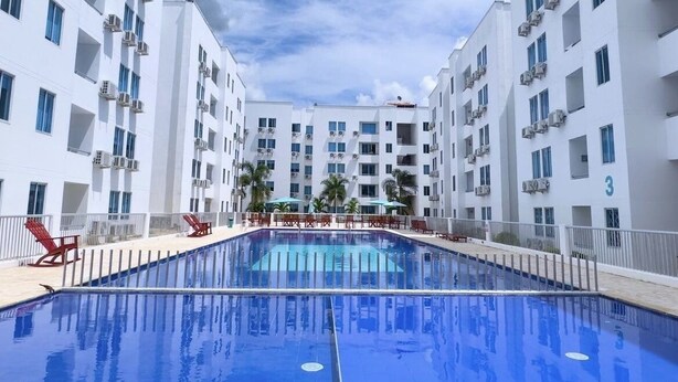 Une piscine entourée de bâtiments blancs dotés de balcons, de palmiers et de chaises longues rouges.