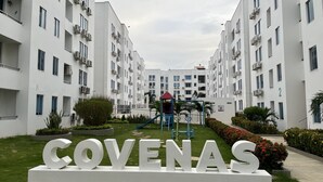 Un immeuble d’appartements moderne doté d’une cour intérieure, d’un espace de jeux pour enfants et d’une grande enseigne « COVENAS ».