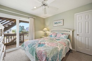 A bedroom with a bed, a ceiling fan, a nightstand, a lamp, a door, and a view of the outside. - 5416- Dragonfly, Ocean Views, Across The Road From Beach, Private Pool, Bring The Pooch! (Nags Head)