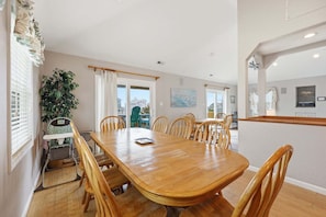 A dining area with a wooden table and chairs, a plant, and a view of the outside. - 5416- Dragonfly, Ocean Views, Across The Road From Beach, Private Pool, Bring The Pooch! (Nags Head)
