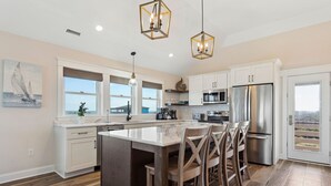 A modern kitchen with a central island, stainless steel appliances, and large windows. - Endless Summer: 1-Min Walk Beach, Pool, Hot Tub (Kitty Hawk)