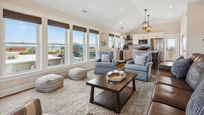 A spacious living room with a large window, a kitchen, and a view of the ocean.