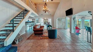 A spacious living area with a staircase, a chandelier, and a view through an archway.