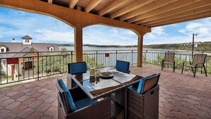 A covered outdoor seating area with a table and chairs, overlooking a body of water and a distant landscape.