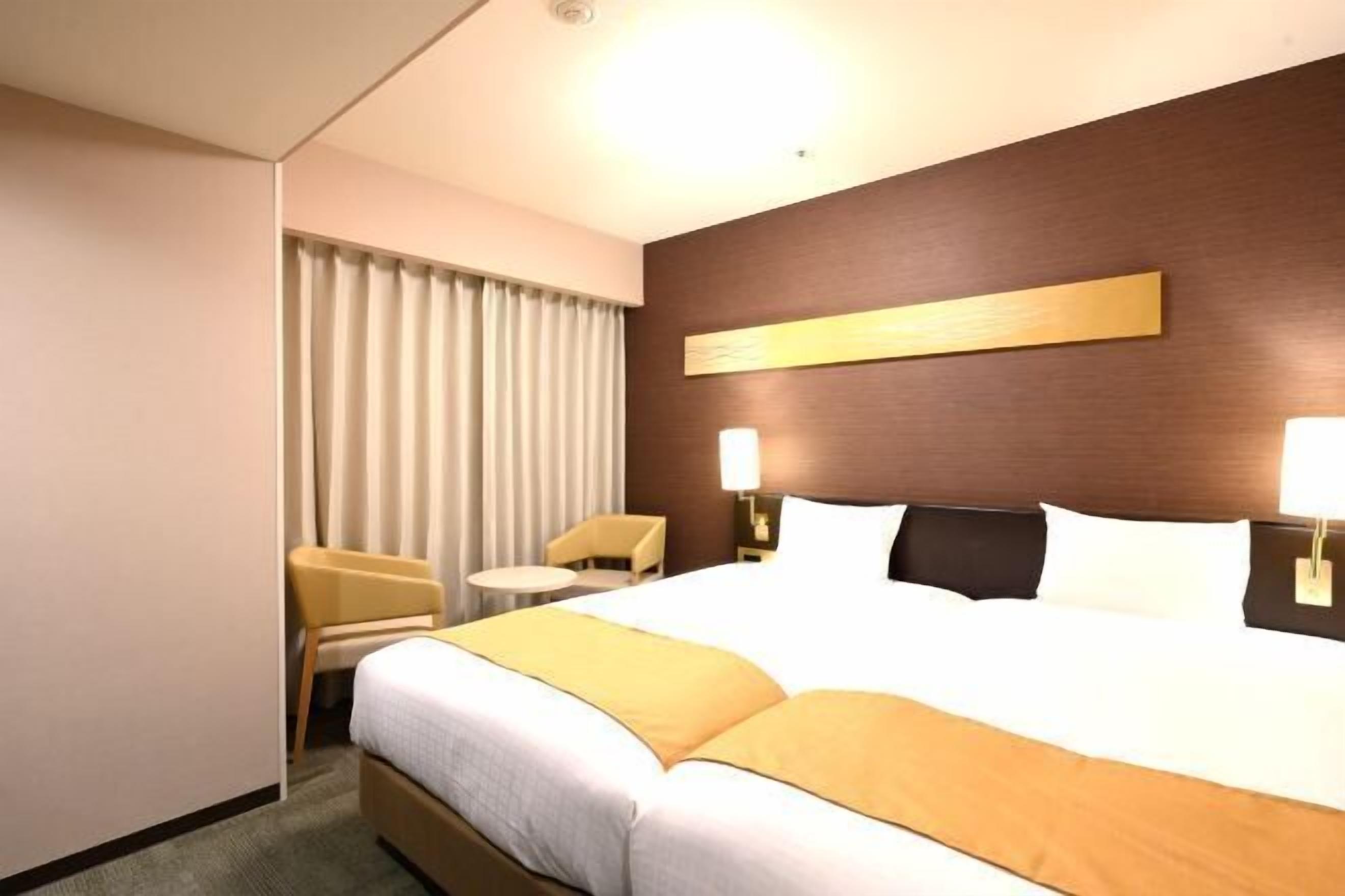 A hotel room with a large bed, a bedside table, a chair, and a window with curtains.