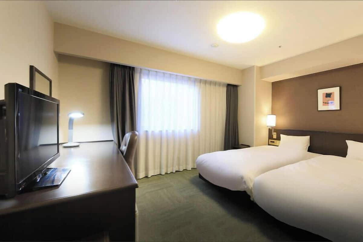 Une chambre d’hôtel avec un lit, un bureau doté d’une télévision, une lampe et un tableau au mur.