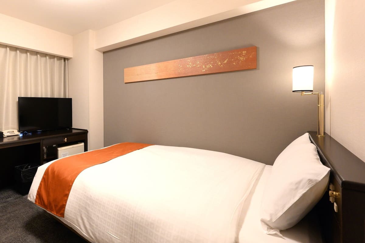 Une chambre d’hôtel équipée d’un lit, d’un téléviseur à écran plat, d’un bureau avec un ordinateur et d’un tableau accroché au mur.