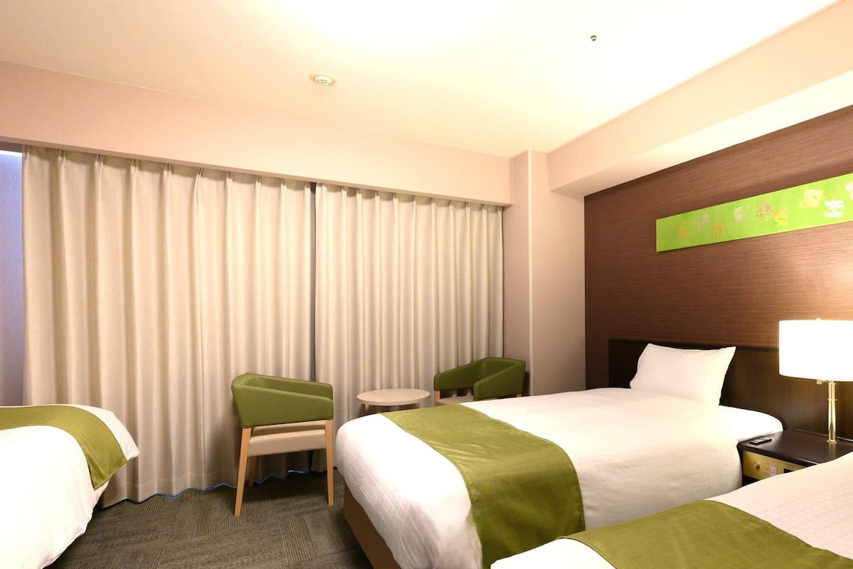Une chambre d’hôtel avec deux lits, une petite table, deux chaises, une lampe et une vue sur les rideaux.