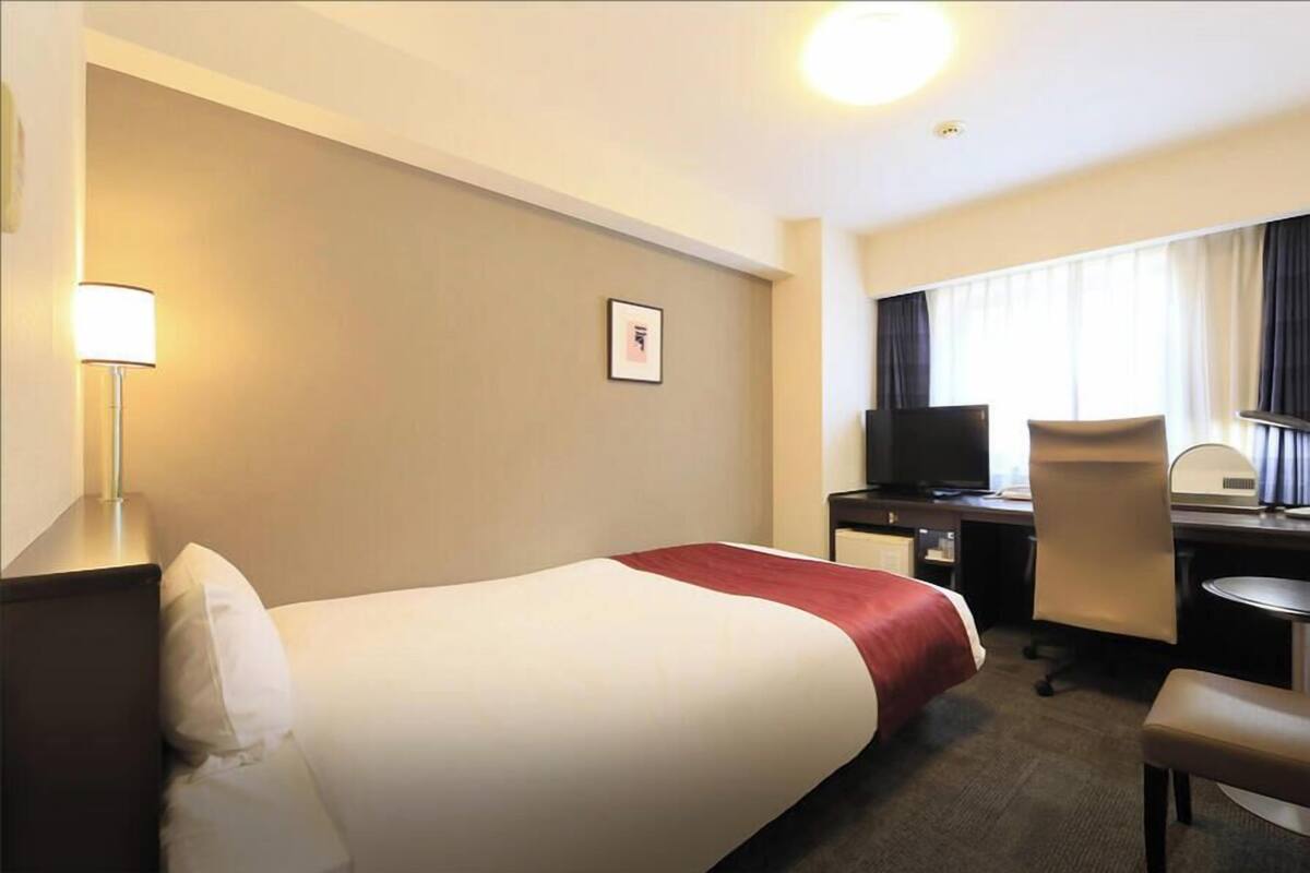 Une chambre d’hôtel équipée d’un lit, d’un bureau, d’une chaise, d’une télévision et d’une lampe.