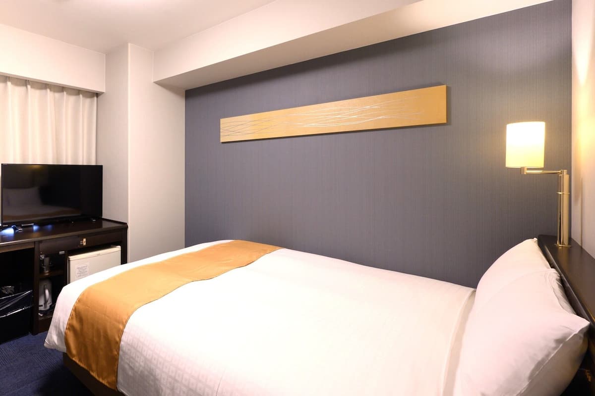 Une chambre d’hôtel équipée d’un lit, d’un téléviseur à écran plat, d’un bureau avec une lampe et d’une œuvre d’art accrochée au mur.