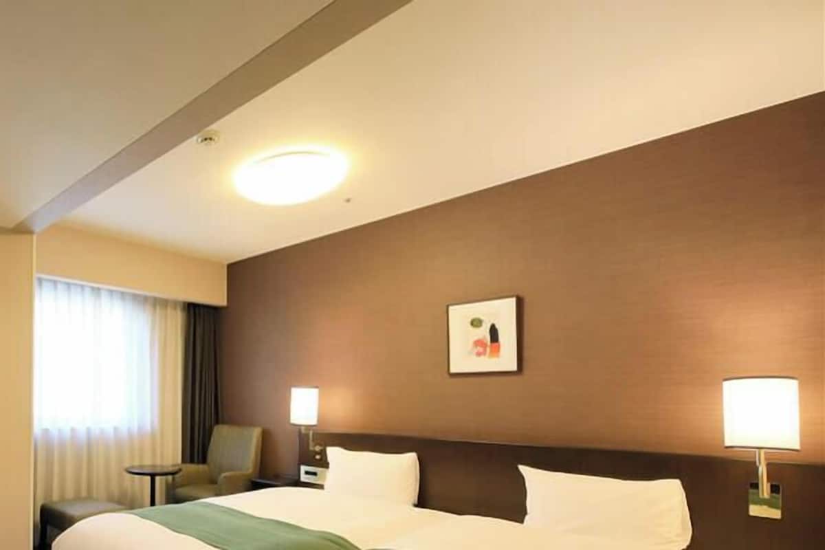 Une chambre d’hôtel avec un lit, des lampes de chevet, une chaise, une petite table et un miroir.