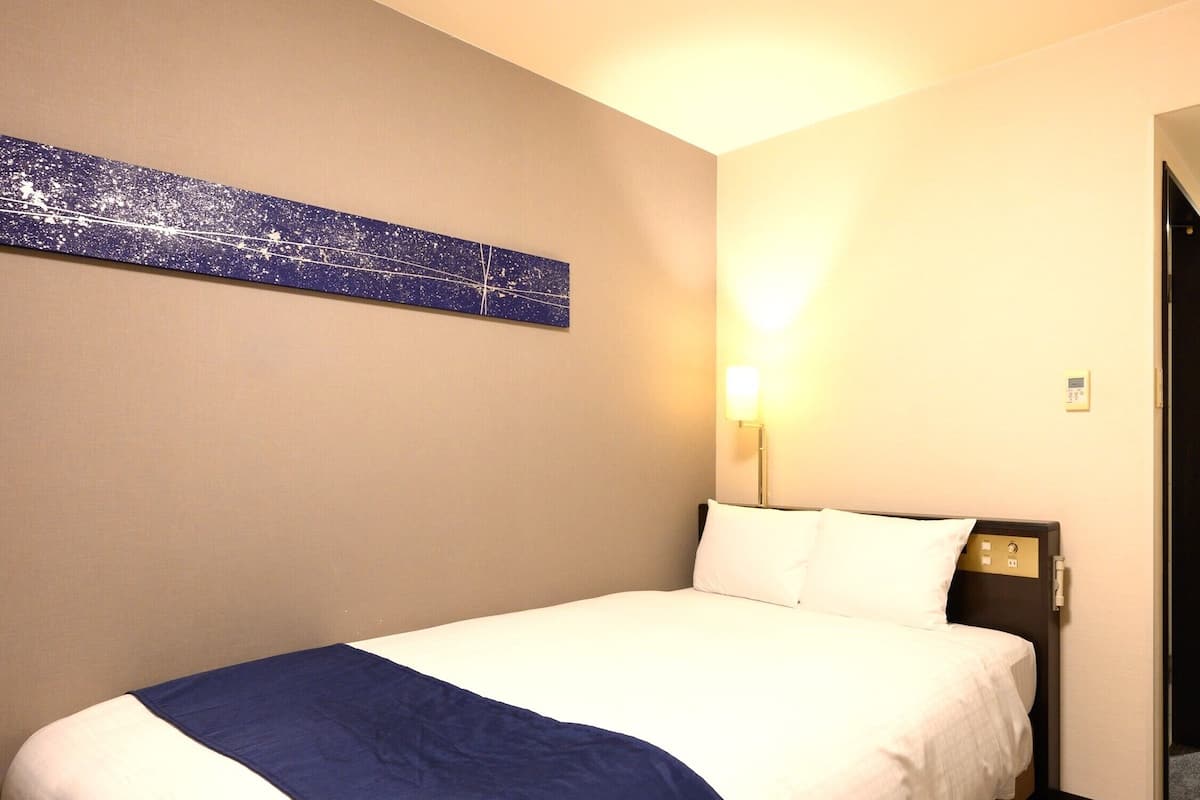 Une chambre d’hôtel avec un lit, une table de chevet, une lampe fixée au mur et un tableau.