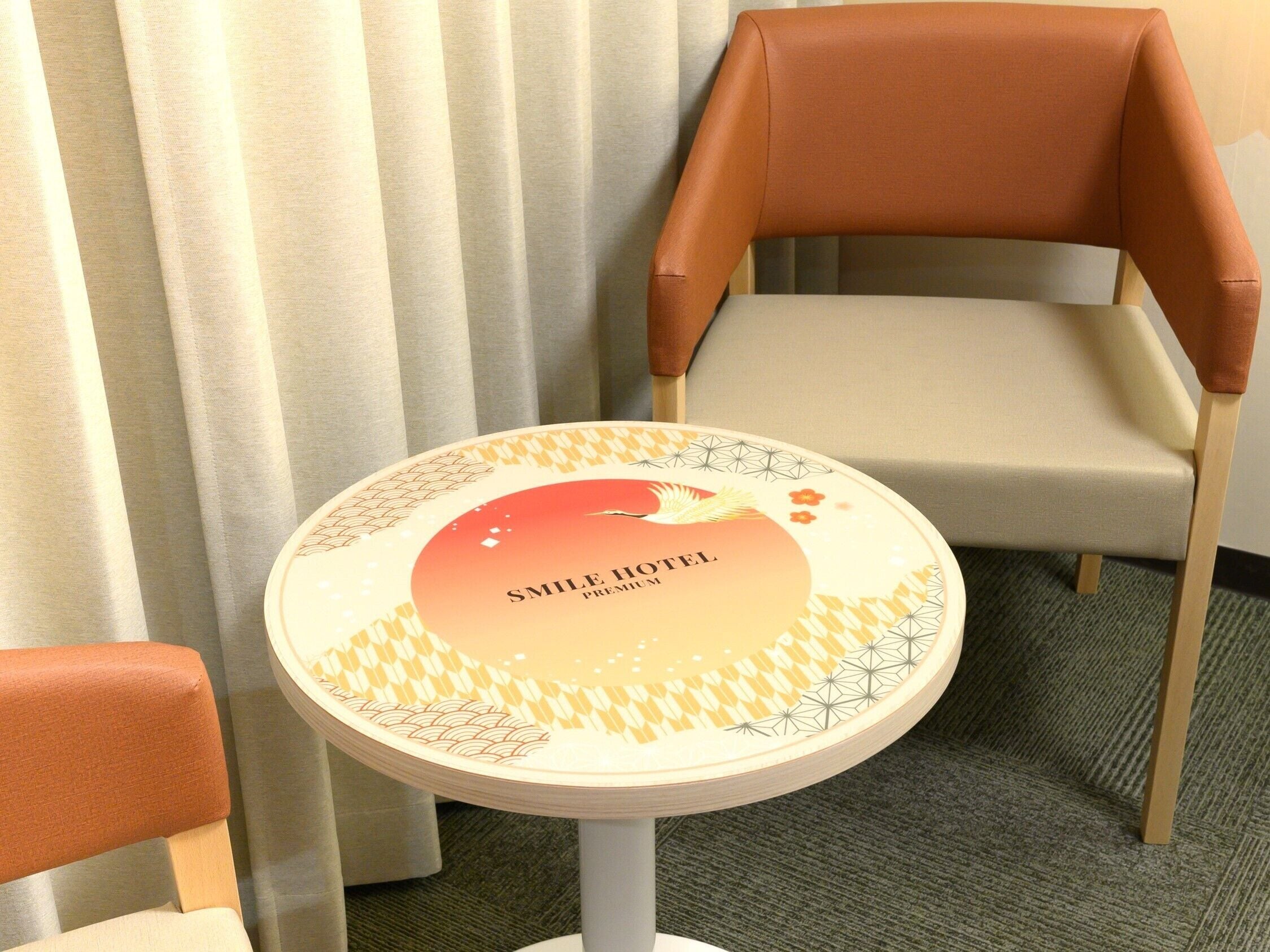 A small round table with a decorative label reading "SMILE HOTEL PREMIUM" in front of a pair of chairs with wooden legs and cushioned seats.