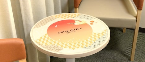 A small round table with a decorative label reading "SMILE HOTEL PREMIUM" in front of a pair of chairs with wooden legs and cushioned seats.