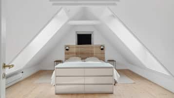 Une chambre avec un plafond en pente, un lit doté d’une tête de lit en bois, deux tables de chevet et un radiateur.