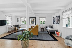 Ein gerÀumiges Wohnzimmer mit einer Couch, Sesseln, einem Couchtisch und einem Fernseher.