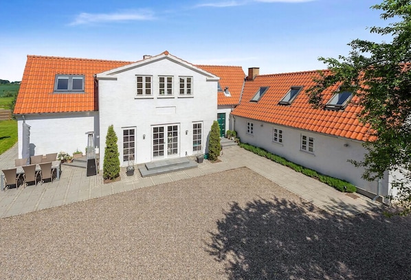 Ein zweigeschossiges Haus mit rotem Ziegeldach, einem Schotterweg und einer kleinen Terrasse mit Gartenmöbeln.