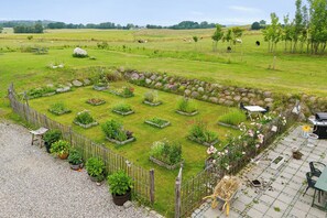Un jardin avec des plates-bandes surélevées, une clôture en bois et un espace patio aménagé avec du mobilier d’extérieur.