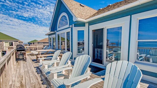 Une terrasse avec des fauteuils Adirondack, un barbecue et une vue sur l’océan.