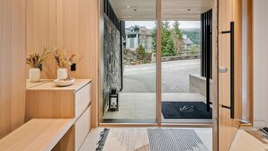 A modern interior with a wooden bench, a small table with decorative items, and a sliding glass door leading to a covered outdoor area. - Blueberry Hill Retreat | Luxury, Close to everything, hot tub, incredible views, (Whistler)