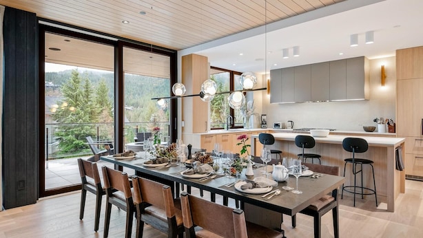 A modern kitchen with a dining area, large windows, and a view of trees. - Blueberry Hill Retreat | Luxury, Close to everything, hot tub, incredible views, (Whistler)