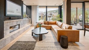 A modern living room with a sectional sofa, a coffee table, a fireplace, and large windows offering a view of the outdoors. - Blueberry Hill Retreat | Luxury, Close to everything, hot tub, incredible views, (Whistler)