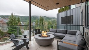 A modern outdoor living space with a fire pit, grey sofas, and chairs, overlooking a mountainous landscape. - Blueberry Hill Retreat | Luxury, Close to everything, hot tub, incredible views, (Whistler)