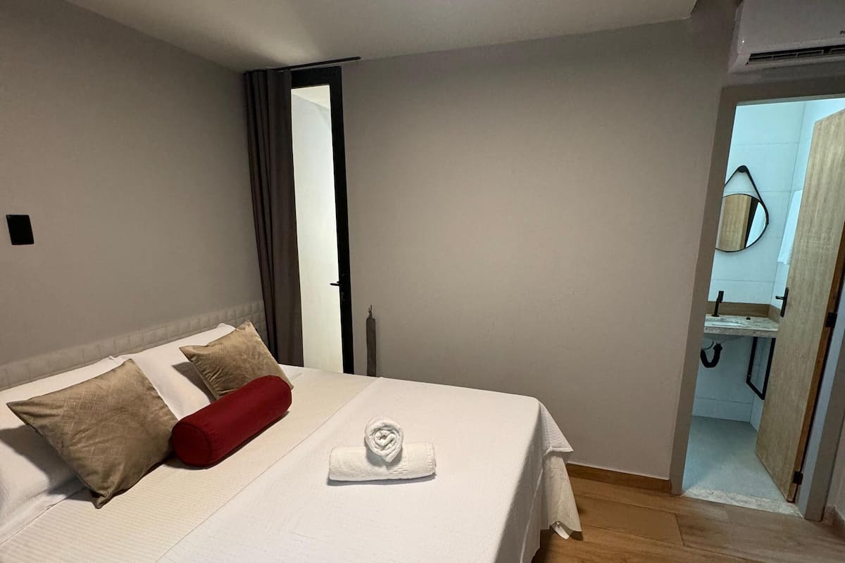 A bedroom with a bed, pillows, a towel, and a wooden floor.