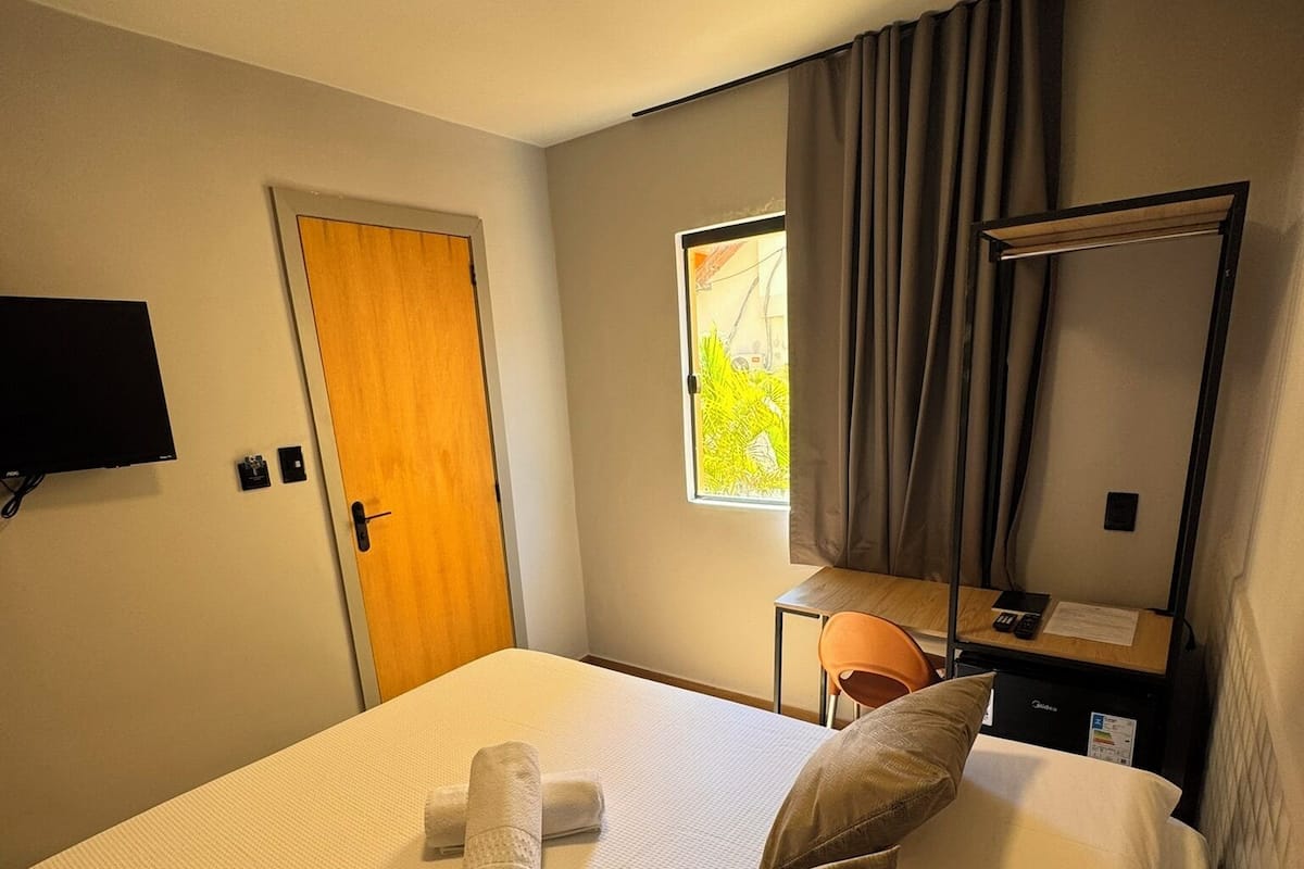 A hotel room with a bed, a desk, a chair, a TV, and a window with curtains.