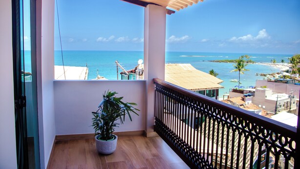 Un balcon avec vue sur la mer, une plante en pot et un plancher en bois.