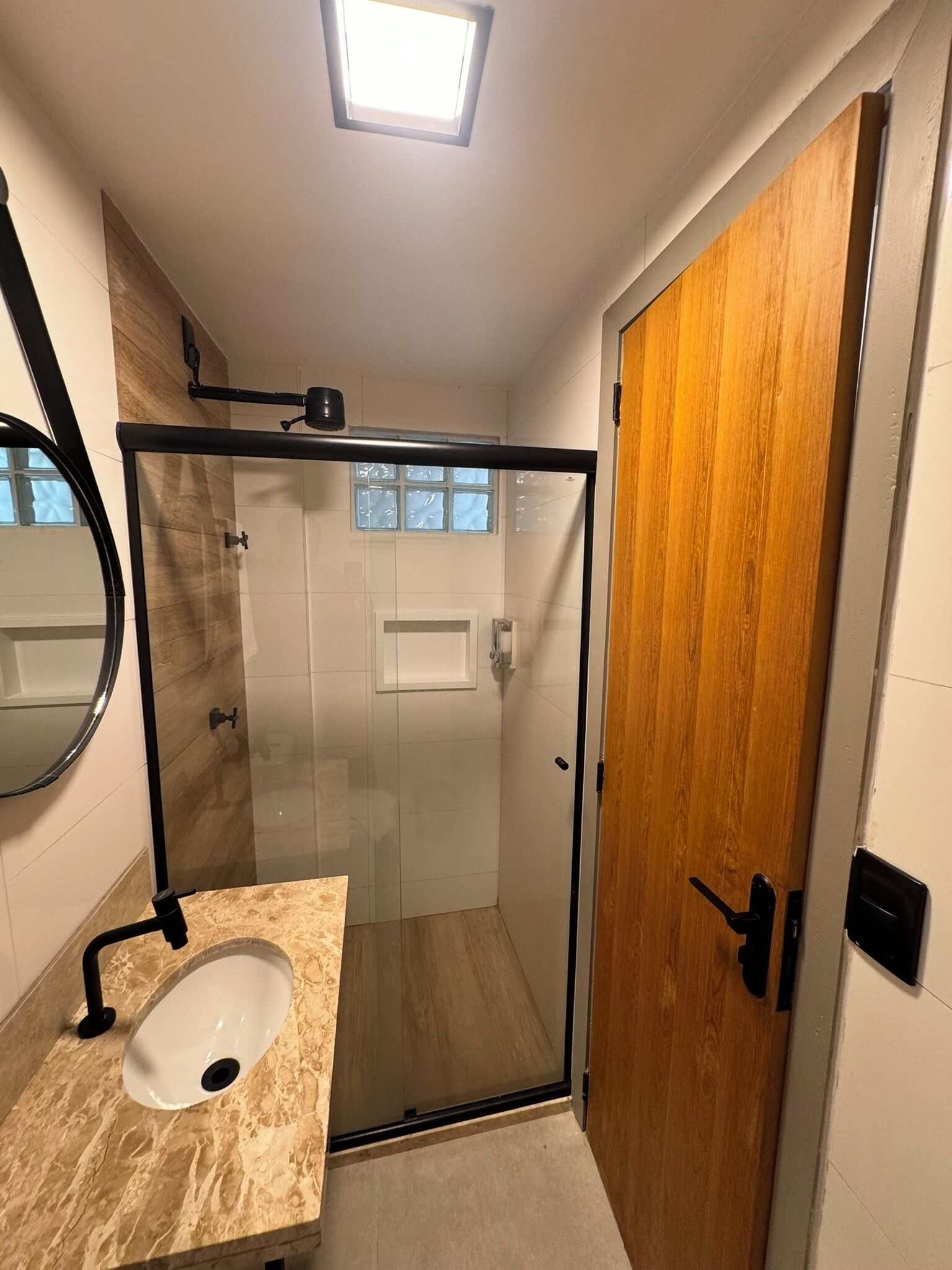 A modern bathroom with a glass shower enclosure, a marble sink, and a wooden door.