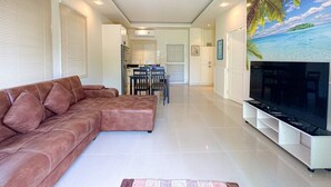 Un salon moderne avec un canapé en cuir marron, un téléviseur à écran plat et un tableau représentant une plage tropicale.