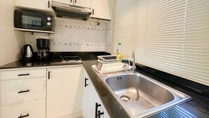 Une cuisine compacte avec des meubles blancs, un four à micro-ondes, une machine à café et un évier.