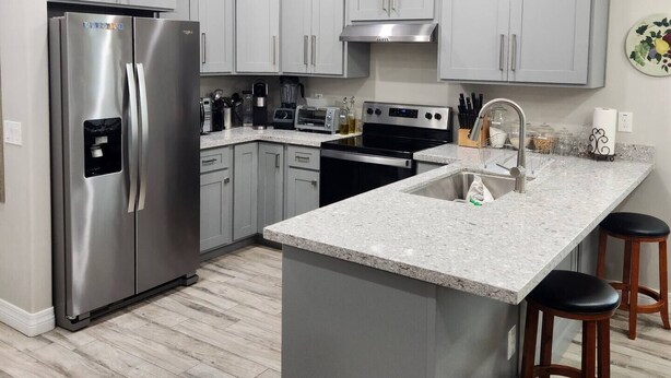 Una cocina moderna con gabinetes grises, electrodomésticos de acero inoxidable, encimera de granito y una isla central con taburetes.