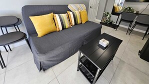 Ein modernes Wohnzimmer mit einem grauen Sofa, gelben Kissen, einem schwarzen Couchtisch und zwei schwarzen Sesseln.