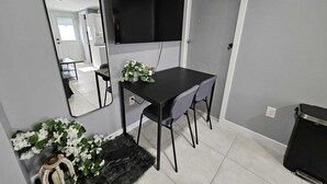 Ein kleiner, moderner Raum mit einem schwarzen Schreibtisch, zwei Stühlen, einem an der Wand befestigten Flachbildfernseher, einem Spiegel und einer kleinen Topfpflanze.