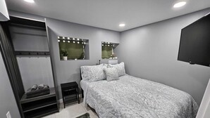 Ein Schlafzimmer mit einem Bett, einem Schminktisch mit Spiegel, einem kleinen Tisch und einem an der Wand montierten Fernseher.