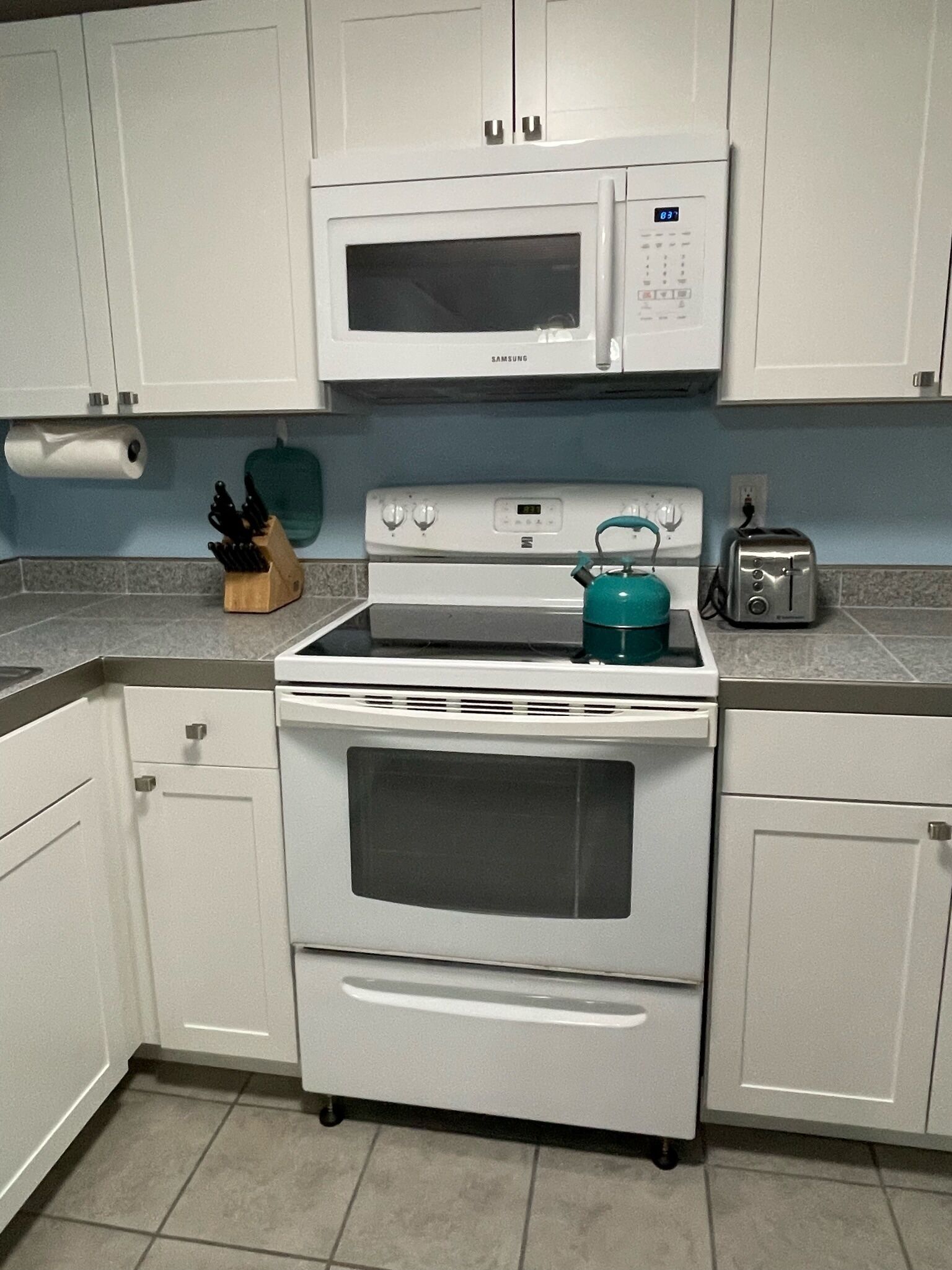 A kitchen with white cabinets, a microwave, a stove, a toaster, and a roll of paper towels.
