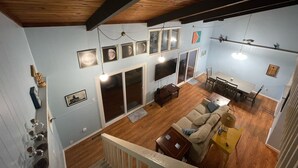 A spacious living area with a wooden ceiling, a sofa, a dining table, and a TV mounted on the wall.